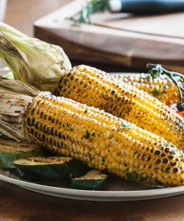 A plate of corn grilled in the husk with zucchini and tomatoes