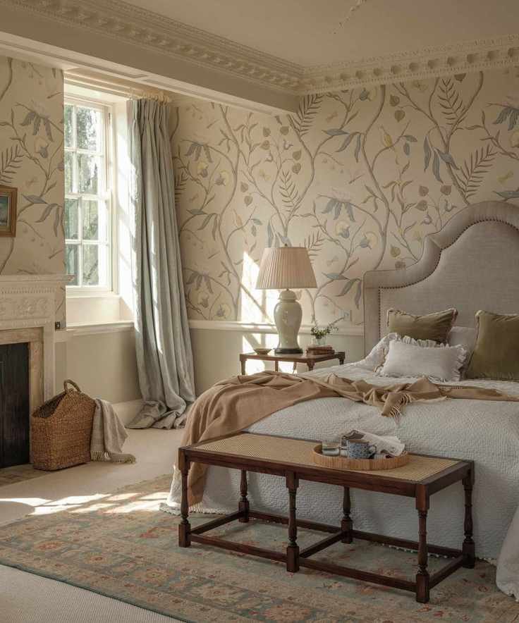 White and beige bedding on a bed with an Anbôise headboard against beige floral wallpaper.