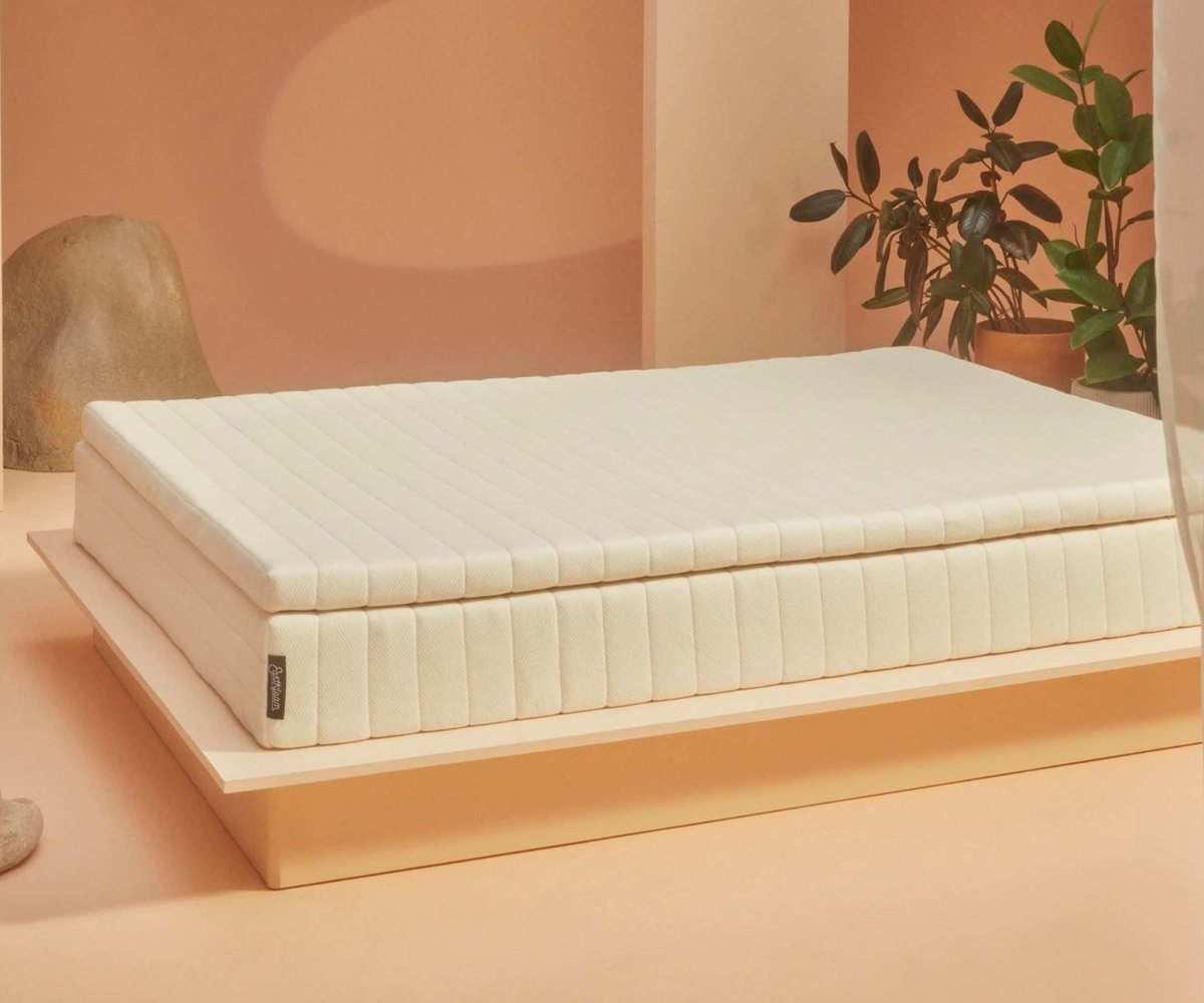 The Earthfoam Mattress Topper on a bed against peach-colored walls, surrounded by plants and decorative rocks.