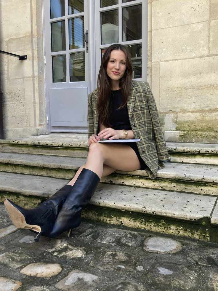 a woman sitting on steps wearing a green jacket, a black dress, and black boots
