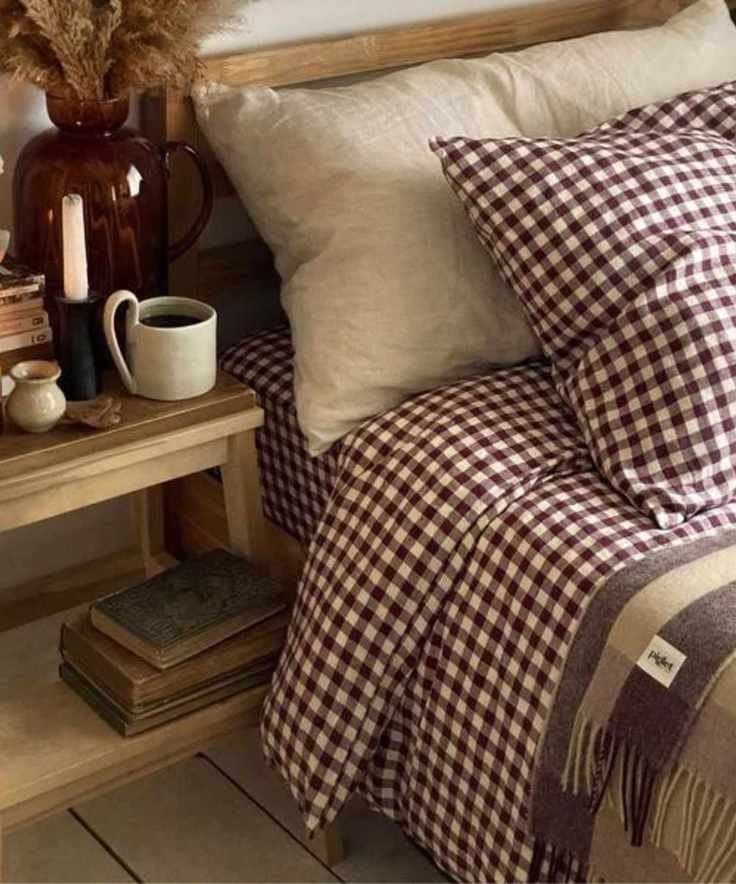 Berry gingham bedding on a bed next to a nightstand piled with candles and books
