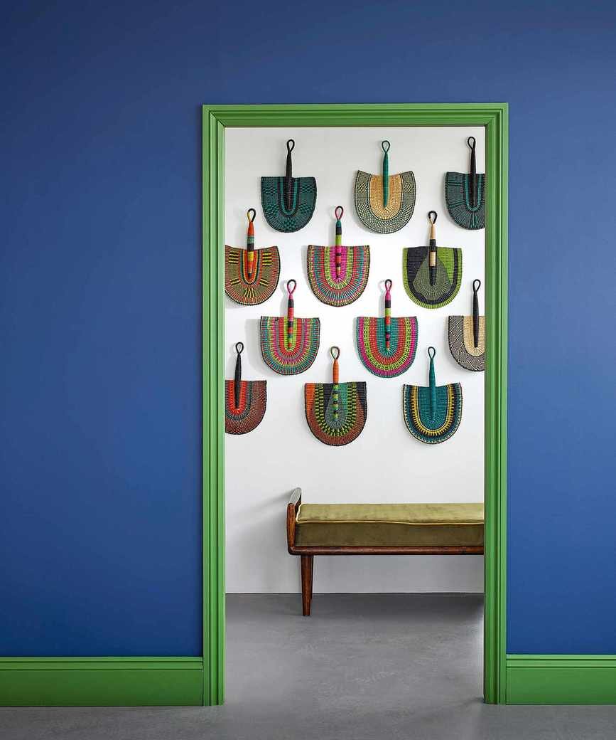 Blue hallway with green painted door frame and gallery wall of fans