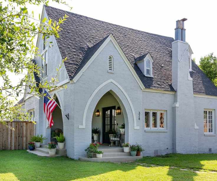 Tudor revival style house with gray painted exterior, arched doorway, grassy lawn