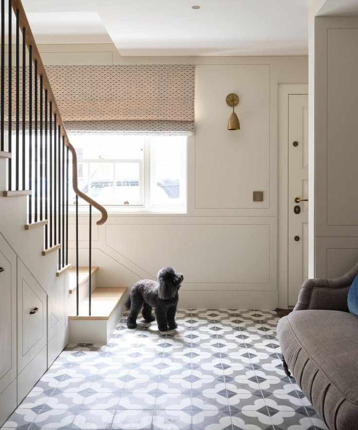 A bright entryway showcasing black and white tiles and stylish decor, with a small poodle nearby.