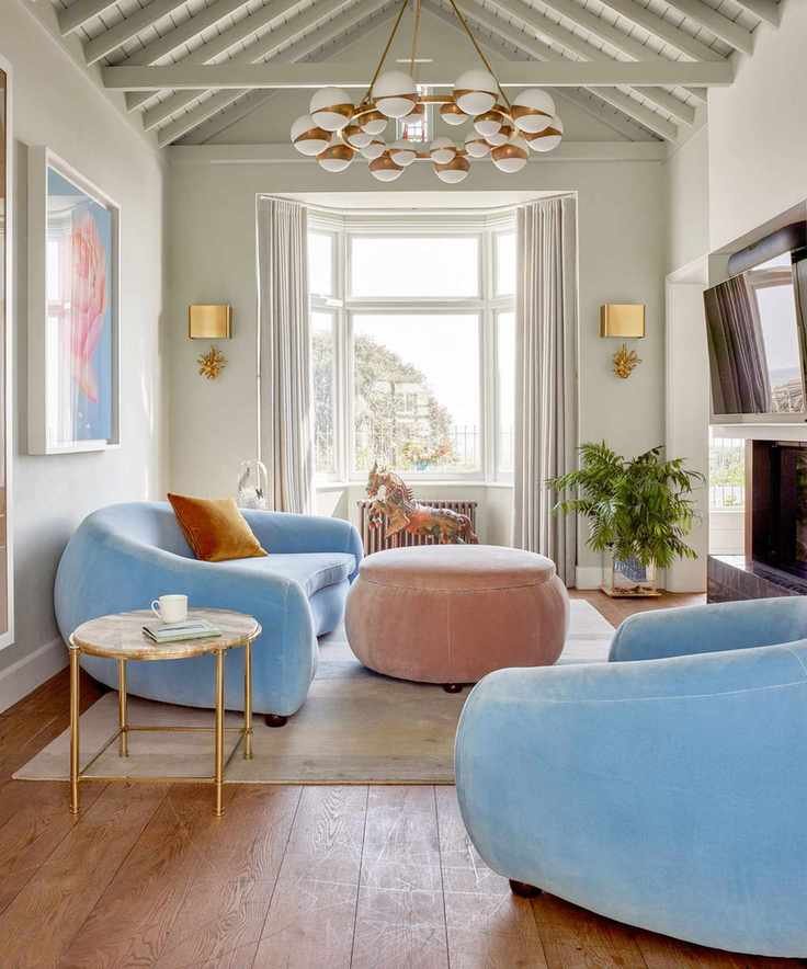 Living room with rounded furniture pieces, pale blue sofa and lounge chair, pale pink ottoman, and dark wood flooring