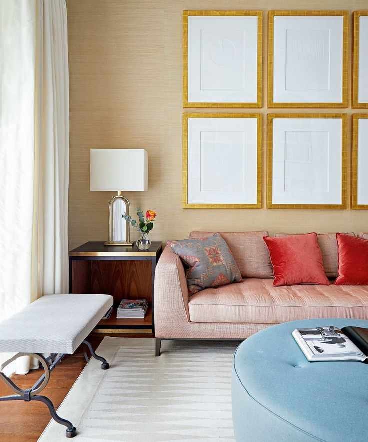 Living room with wallpapered wall, elaborate cornice, red sofa and large circular ottoman.