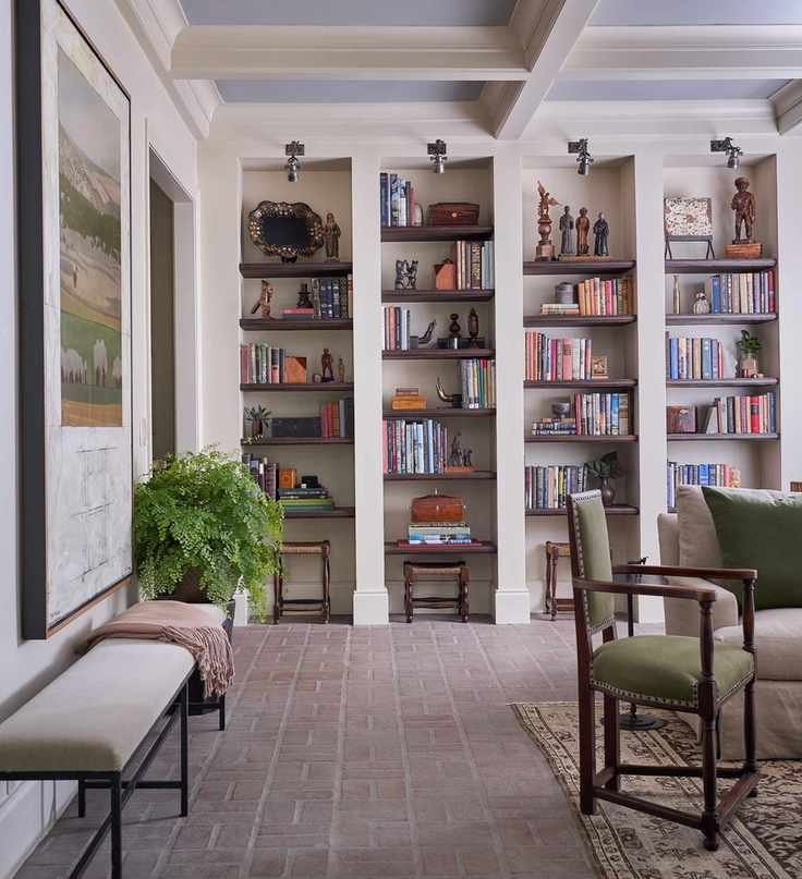 Living room with terracotta floor, built in shelving, neutral walls, bench, armchair and sofa