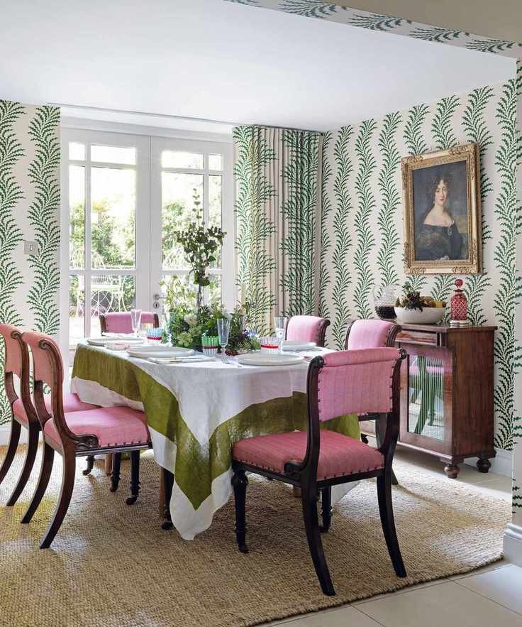Dining room with bold foliage wallpaper and pink dining chairs.
