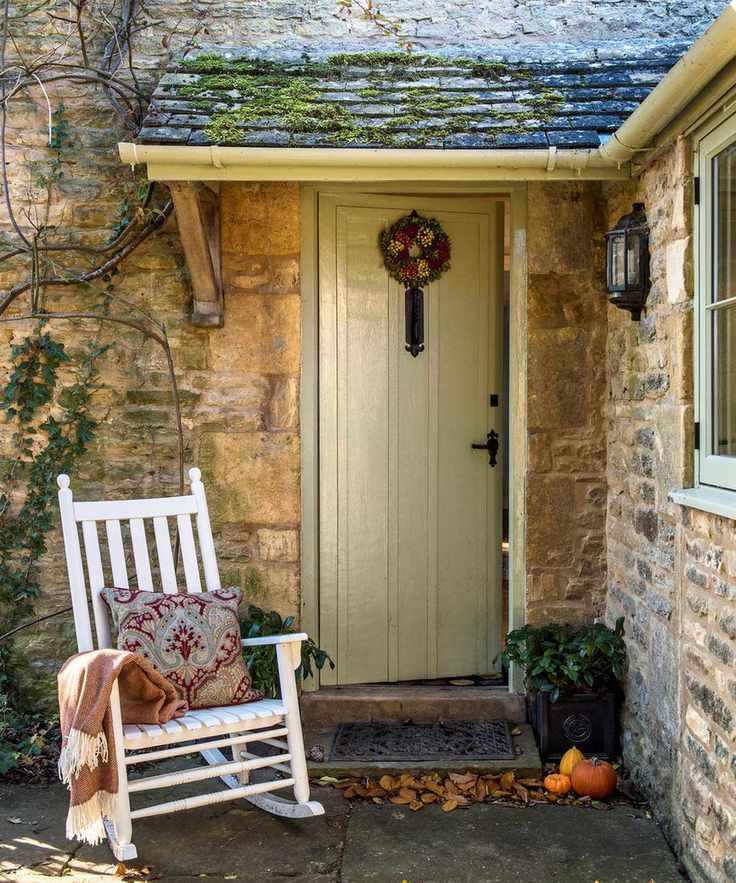 An example of front porch lighting ideas showing a green front door with a white rocking chair and a wall light