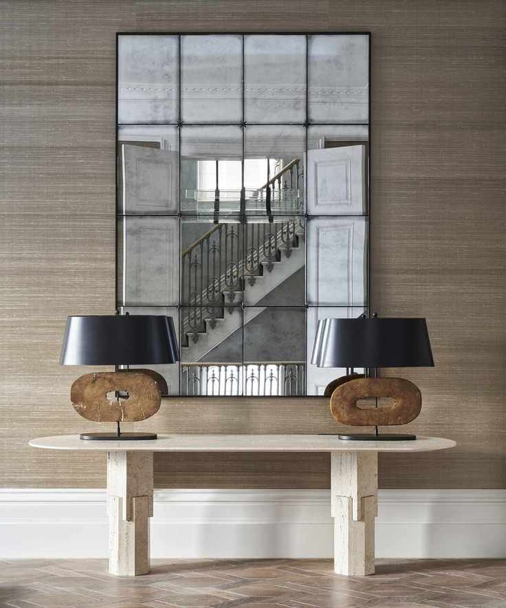 A hallway wallpaper idea with brown grasscloth and large mirror behind entry table with modern lamps