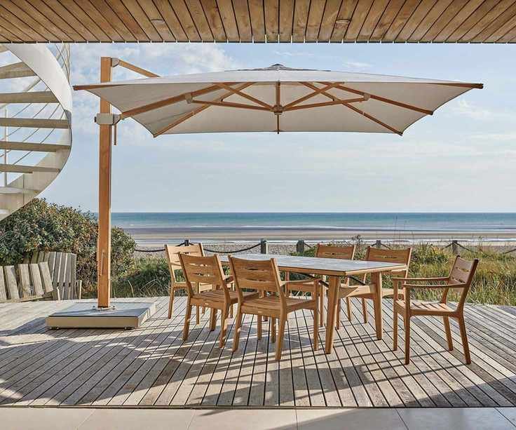 Teak outdoor dining table and chairs under a patio umbrella on a covered patio