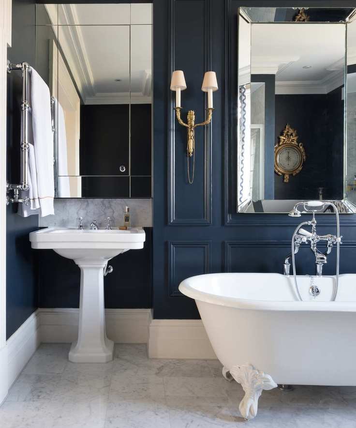 A dark blue paneled bathroom with a traditional white sink and white free-standing bath
