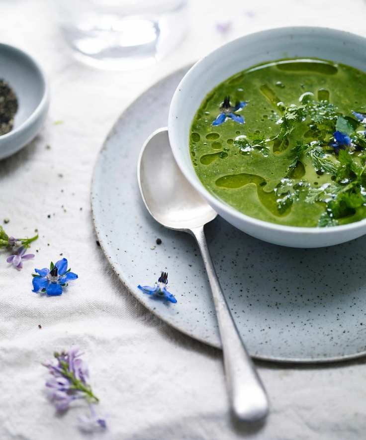 A vibrant green herb soup garnished with edible flowers