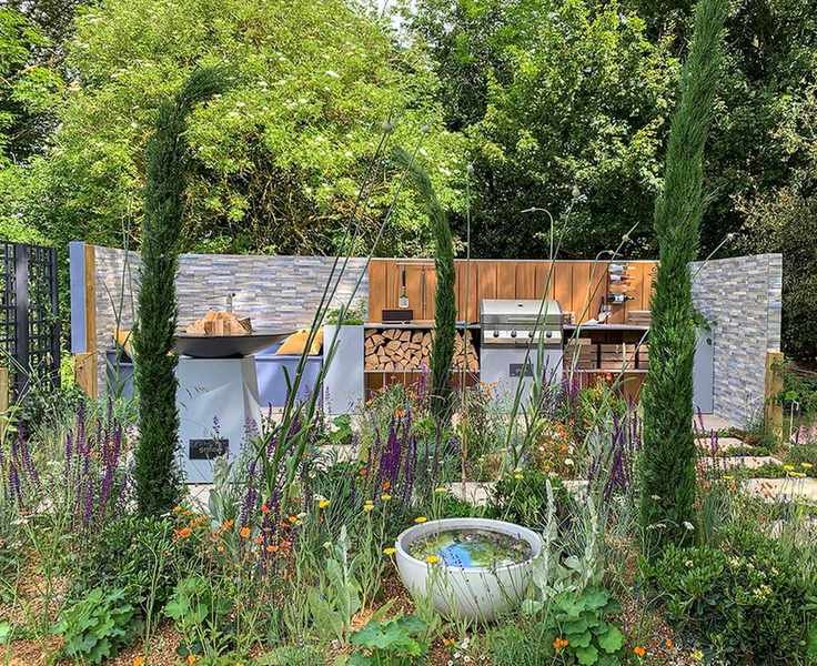How much does an outdoor kitchen cost, explained with a slate-backed design featuring barbecue, fire pit and tall plants.