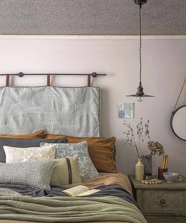 Close up of a bed dressed with coloured blankets and cushions, bedside table with a vase of grasses.