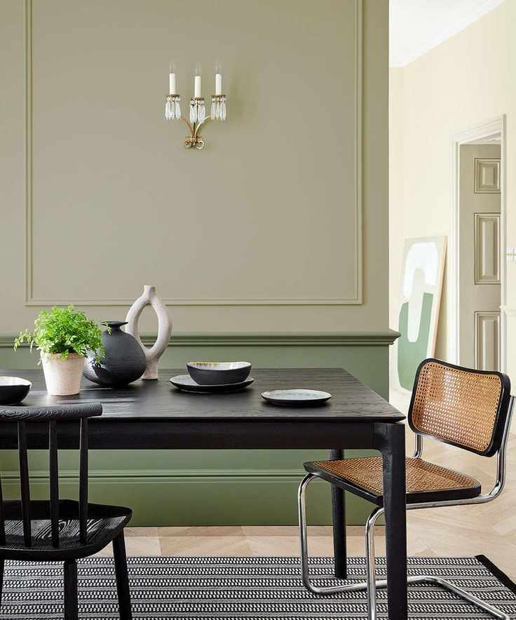 Dining room with two shades of green wall paneling and a black dining table.