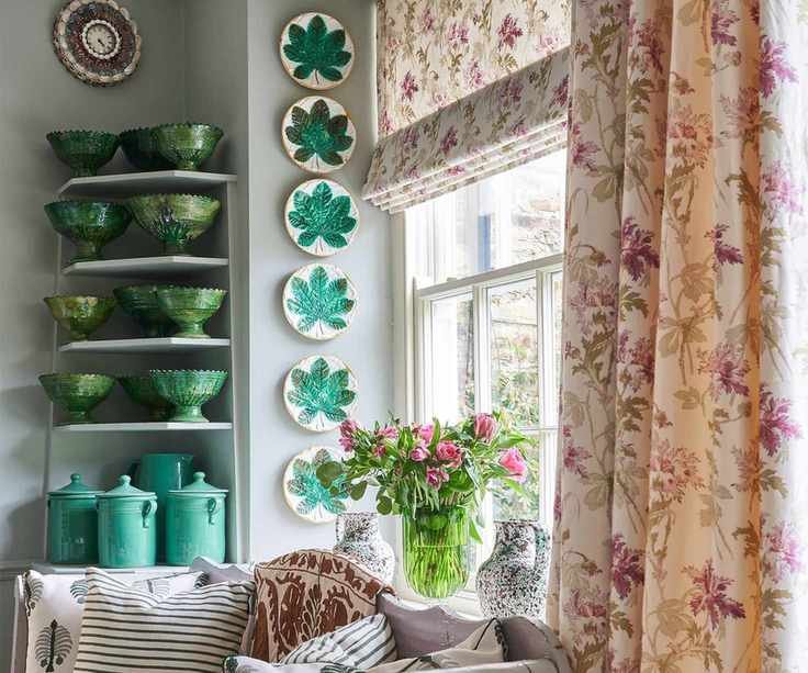 Green ceramics on shelf with plates on wall and day bed and large window with patterned curtains
