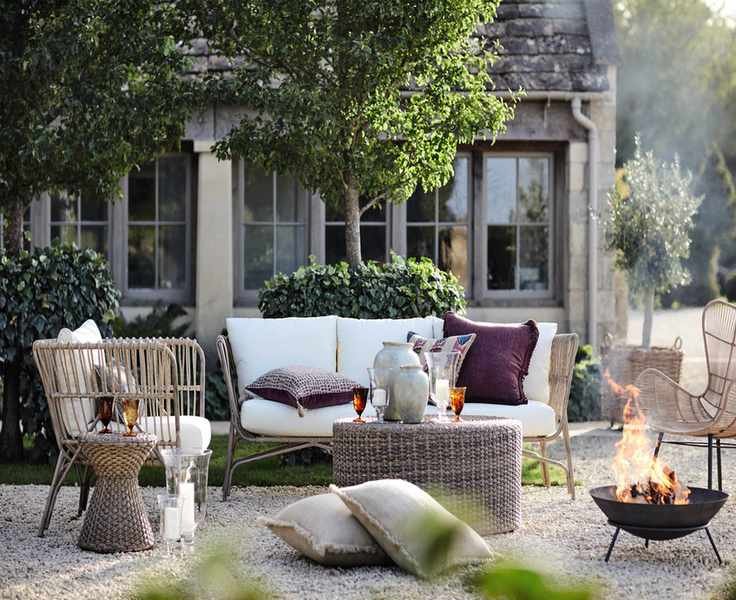 Mismatched wicker outdoor patio furniture ideas with a fire pit in a gravel country-style patio space.