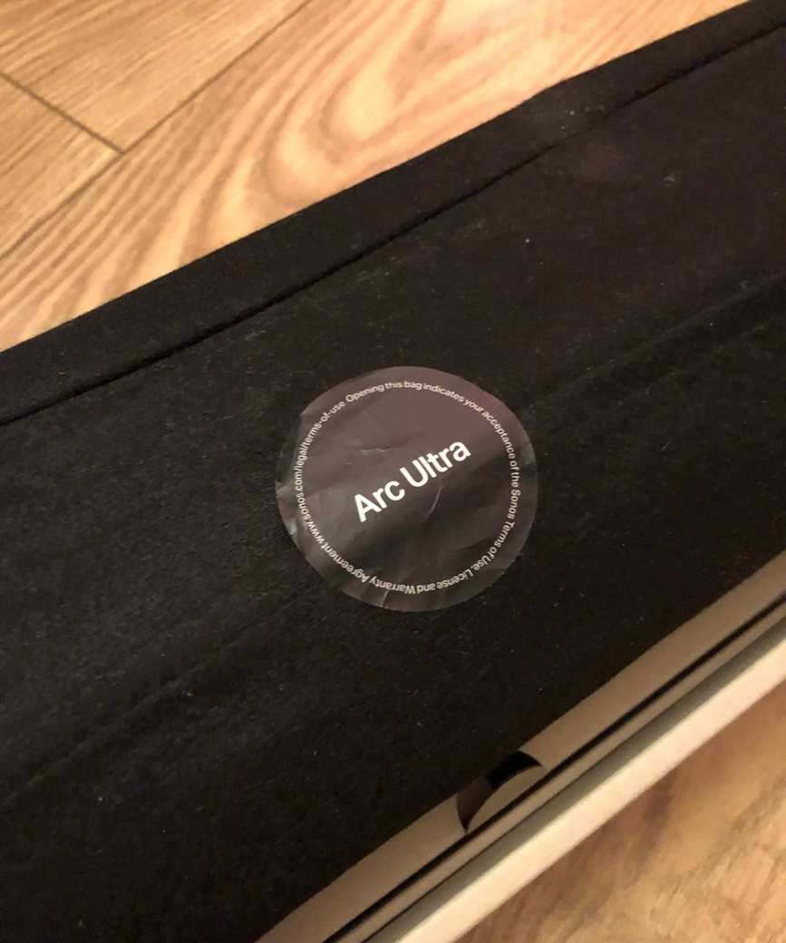 Sonos Arc Ultra in soft, protective sleeve, still in box, on wooden floor in Dan Fauzi's home.