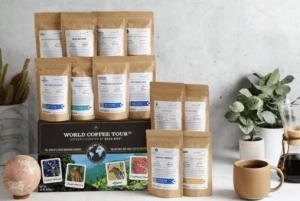 Brown coffee bags are stacked beside a gift box with a cup of coffee and a potted plant in front.