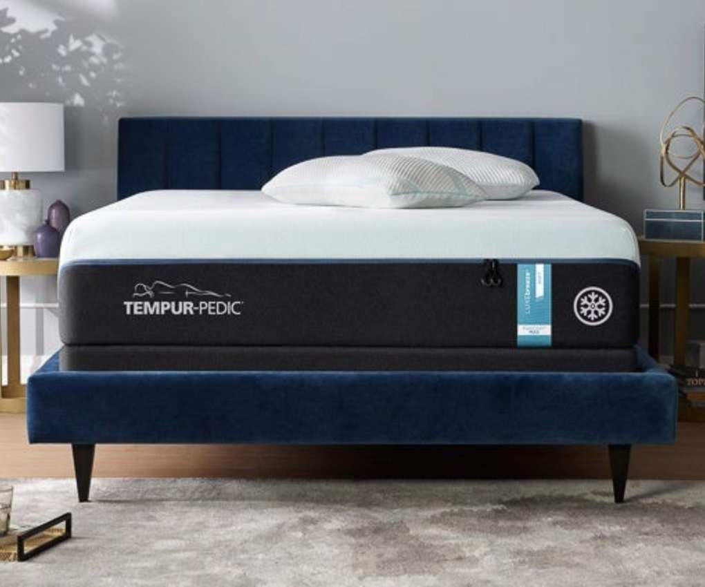 A Tempur-Pedic mattress on a bed against a gray wall.