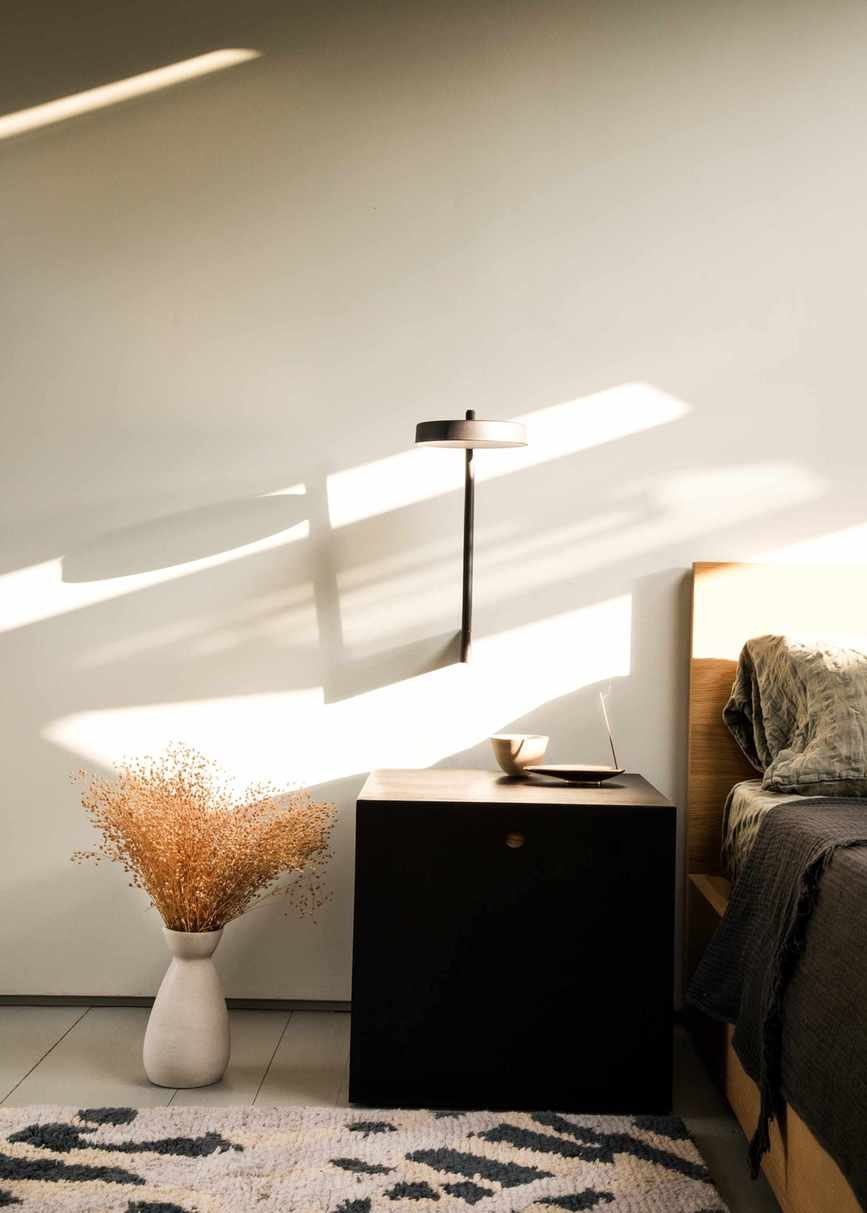 A Mid-Century Modern style bedroom with a wooden bedframe, a dark black nightstand, and a structural lamp sconce on the wall