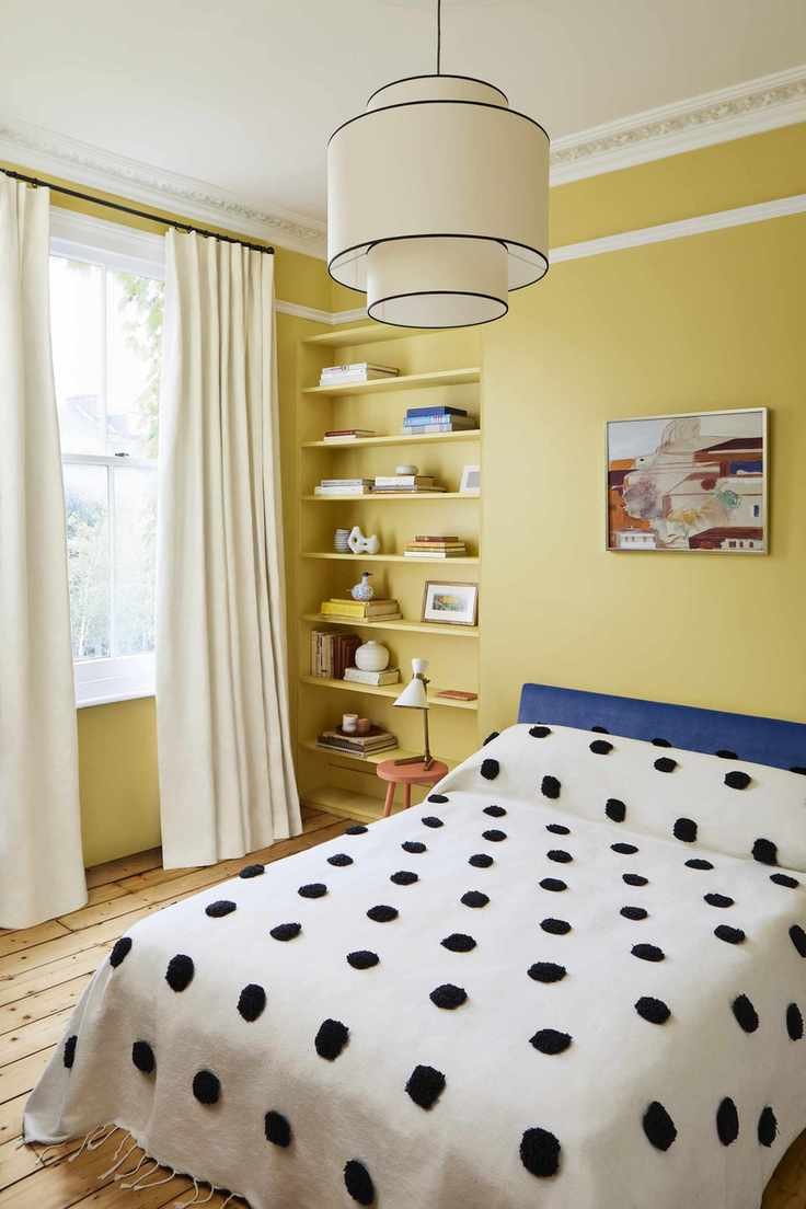 yellow teen girl bedroom with black and white spot blanket, shelving, artwork, wooden floor, blue headboard