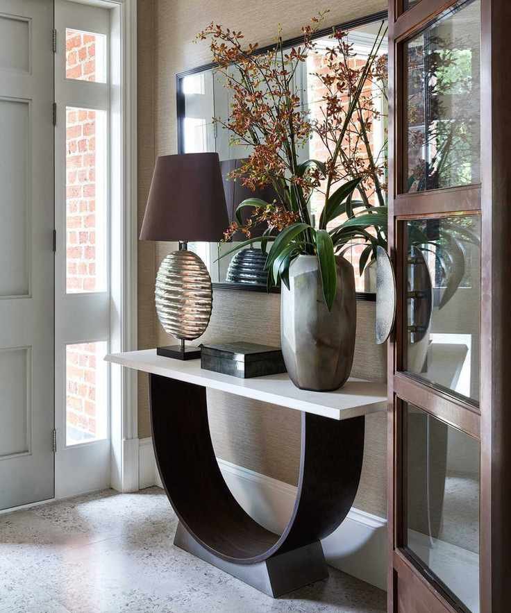 A modern hallway featuring a stylish console table with a curved design, adorned with a lamp and flowers