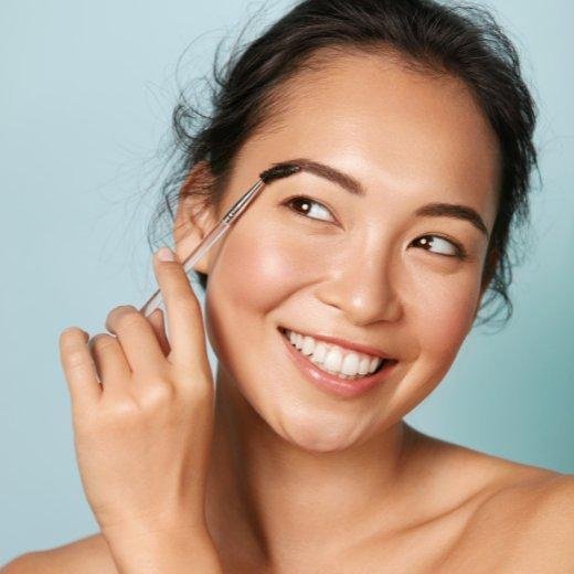 Woman applying moisturizer to eyebrows with a spoolie Woman applying moisturizer to eyebrows with a spoolie