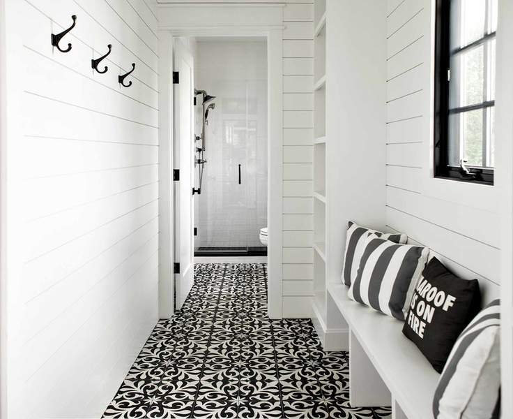 The entrance to a pool bathroom with black and white patterned tile floors and white shiplap walls.