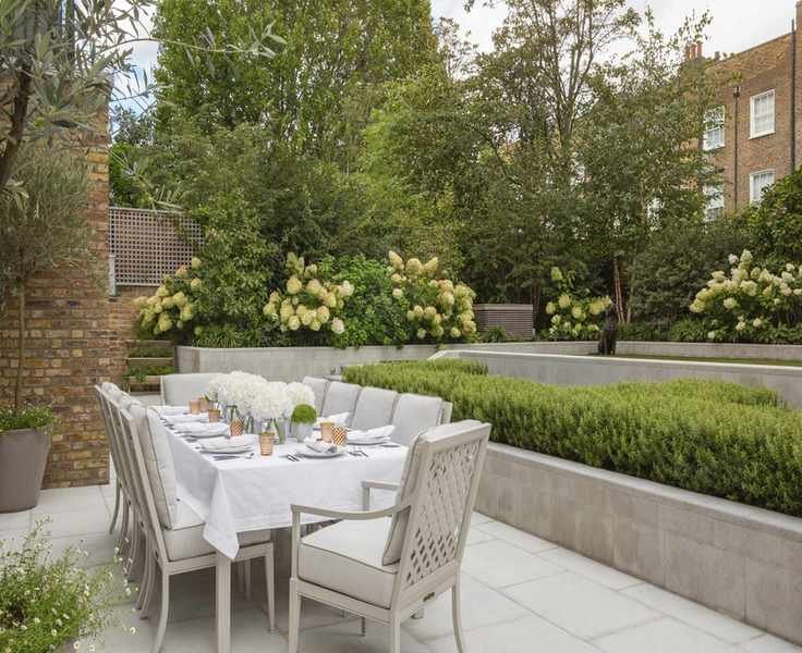 Long table set with white linen in a garden with white hydrangeas.