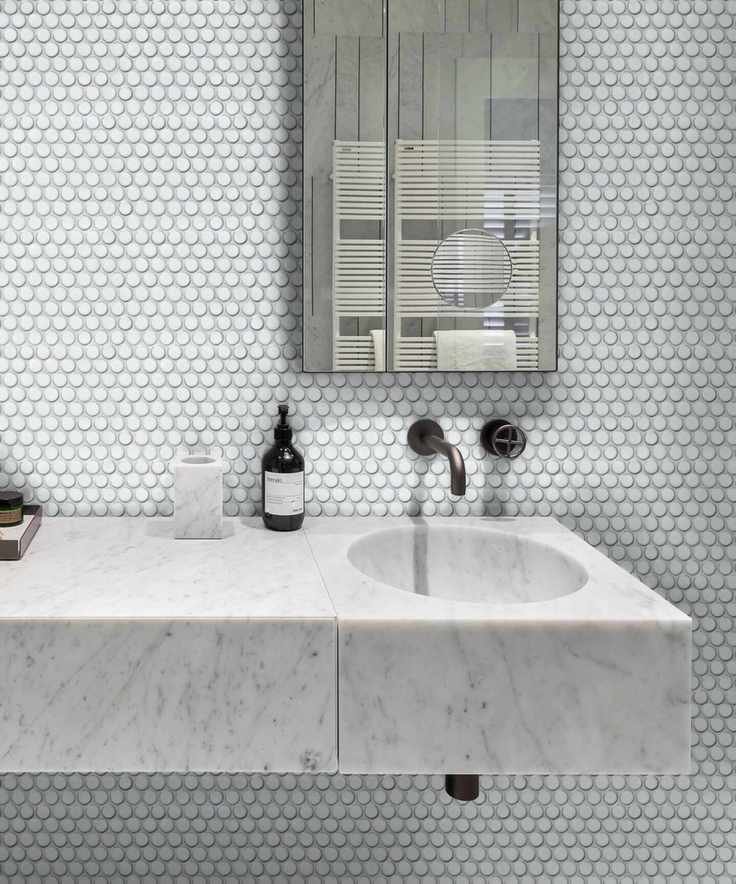 Small white bathroom tiles above a marble sink boost space in a tiny bathroom.