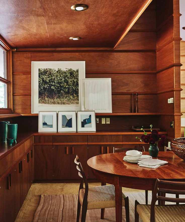 Midcentury dining room with wood panelling, round wood table and prints