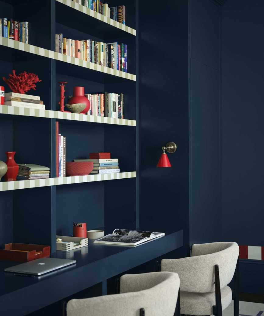 home office with dark blue color-drenched walls, shelving with books and decor, and desk space