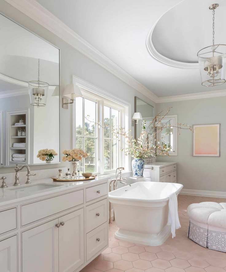 A spacious bathroom with pale blush tile flooring, light gray walls and ceiling, white trim, a freestanding bathtub, and a large white vanity.