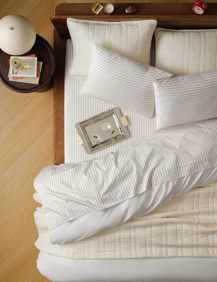 Brooklinen striped luxe sateen bedding and silver martini tray pictured from a bird's eye view inside of a neutral bedroom with hardwood floors