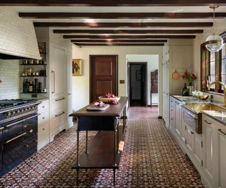 Tudor kitchen with dark beams, tiled floor, subway tiled hood and range oven and cream cabinets