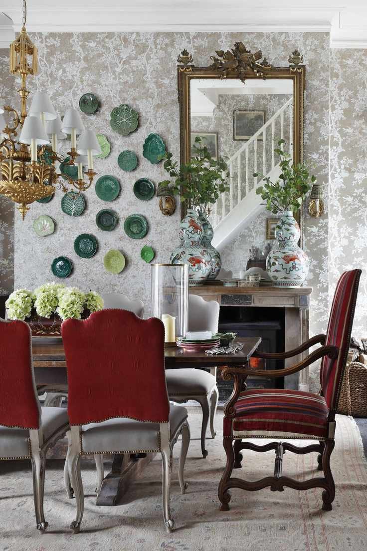 damask style wallpaper in dining room with table setting, ornate mirror, plates on the wall, gold chandelier, upholstered dining chairs