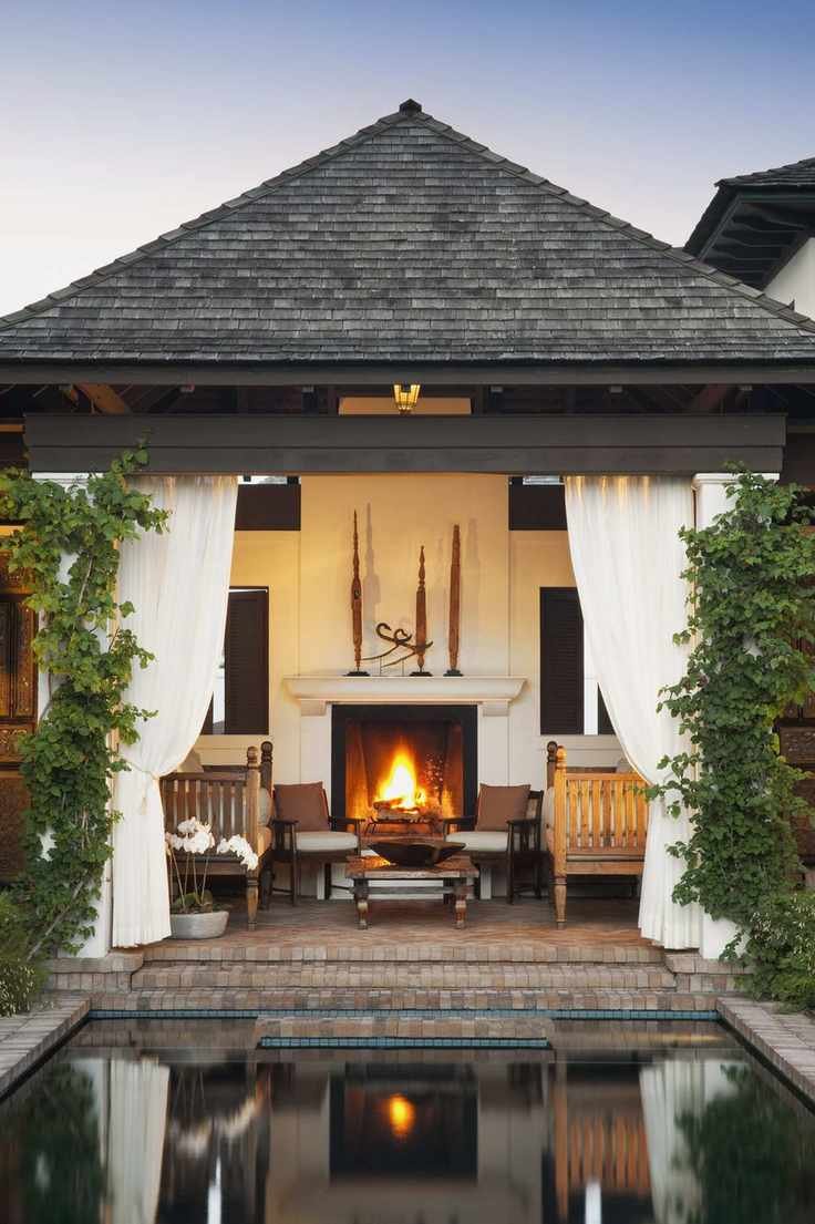 An outdoor porch area with brick steps, a fireplace, garden furniture, and white curtains tied back