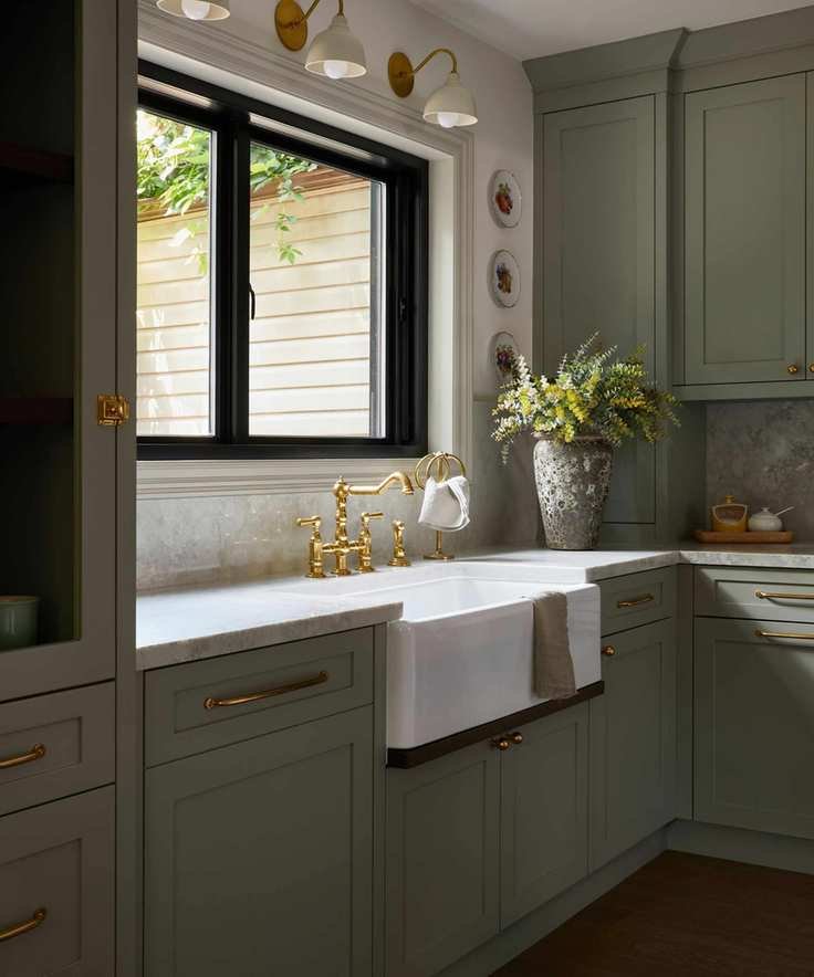 a sage green shaker kitchen sink area with a farmhouse sink and a large window dressed with sconces and wall plates