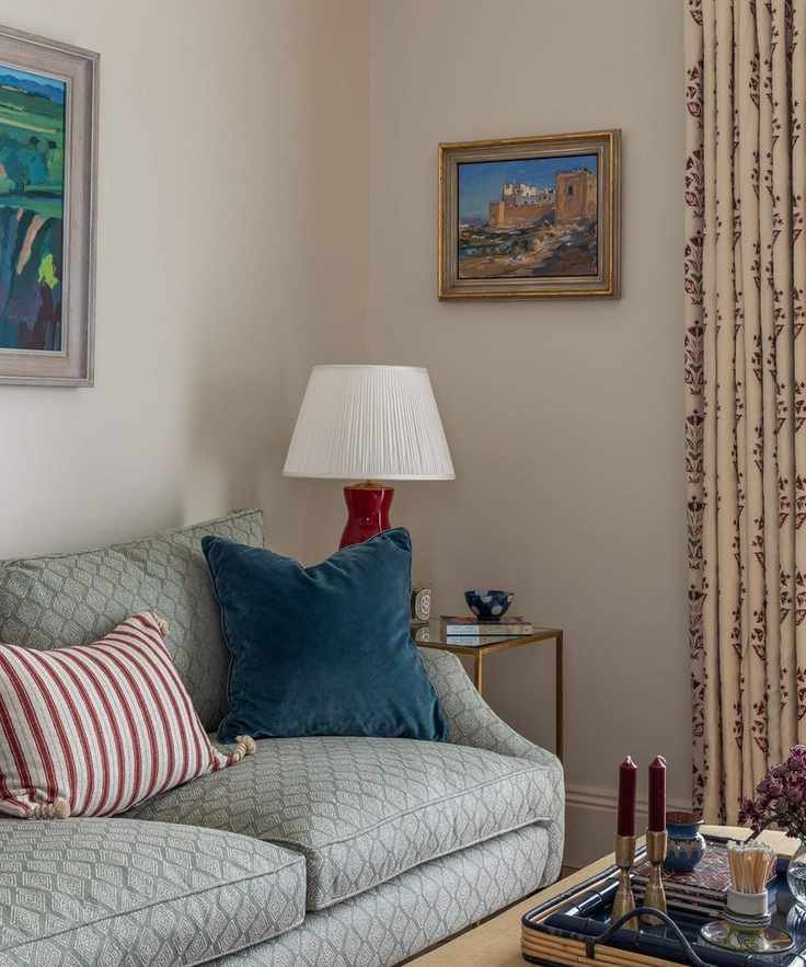 The corner of a living room with creamy beige walls painted in Slipper Satin by Farrow & Ball, featuring a blue sofa and decorative items.