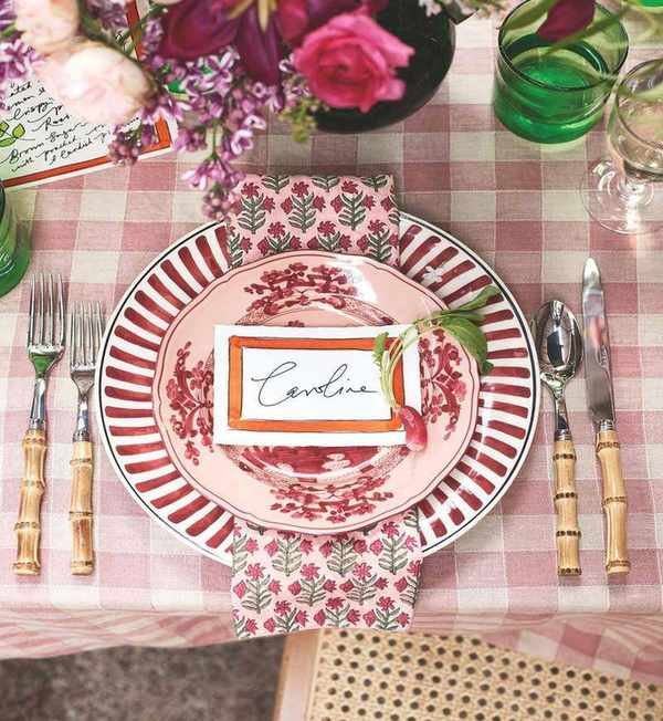 red and white place setting with gingham tablecloth, striped plate and floral napkin with a place card and bamboo cutlery