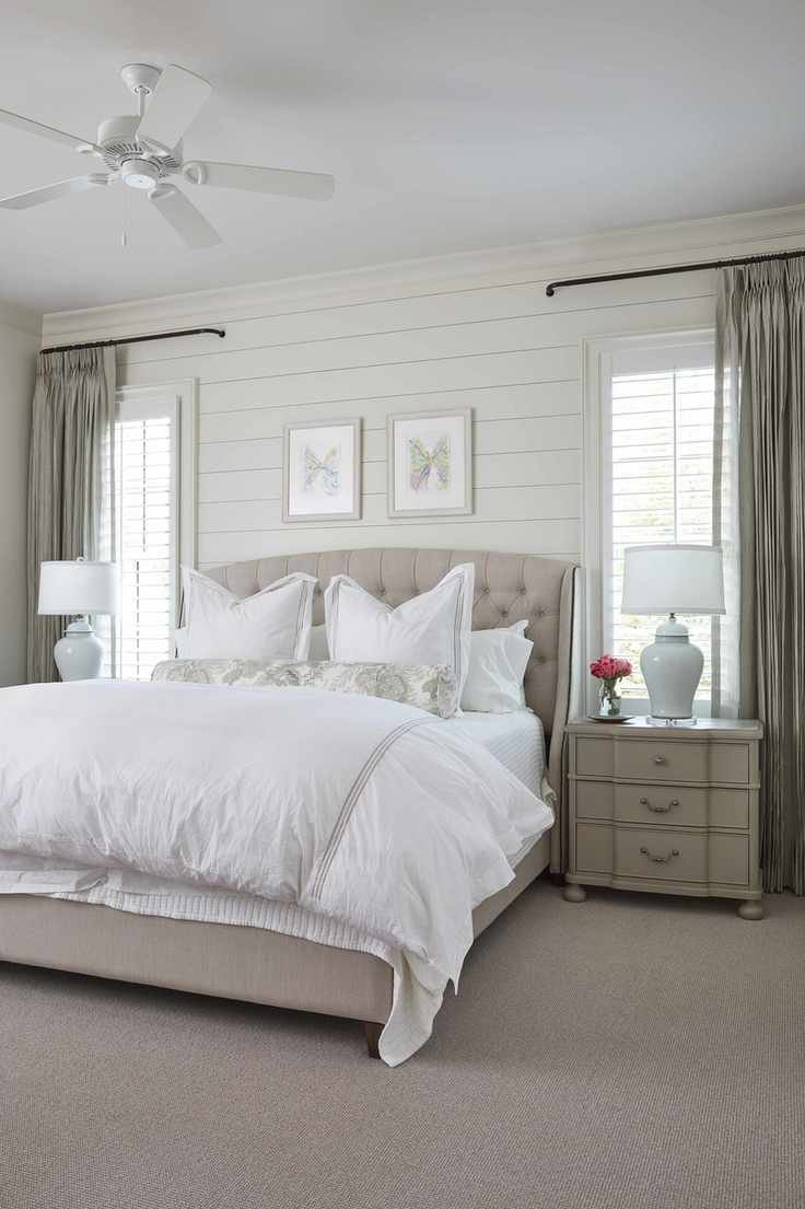 A neutral bedroom with a double bed with white bedding, wall paneling and a light gray carpet
