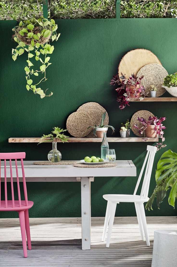 A dark green fence contrasting with white furniture and pink chairs.