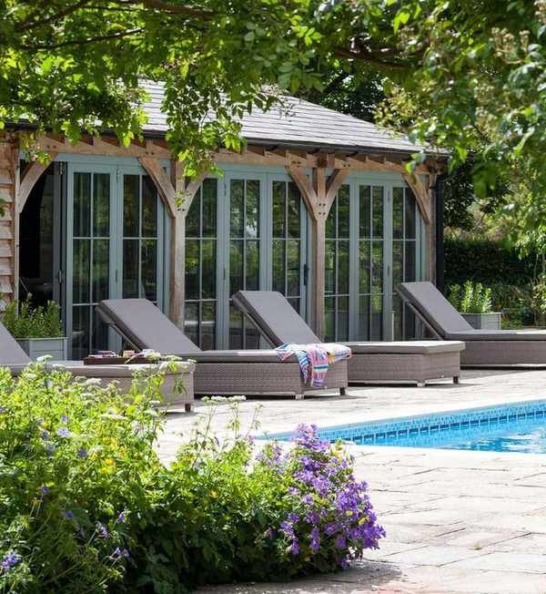 A Mediterranean style garden room surrounded by plants next to a pool area