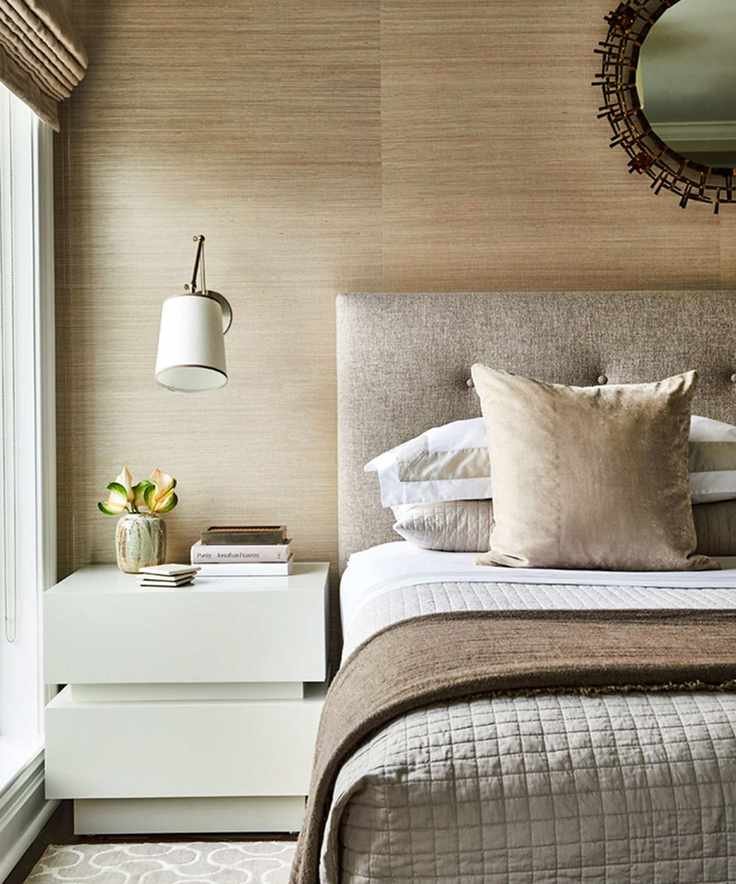 Modern bedroom with neutral brown and beige color scheme. Layered bedding, wall lamp above beside table.