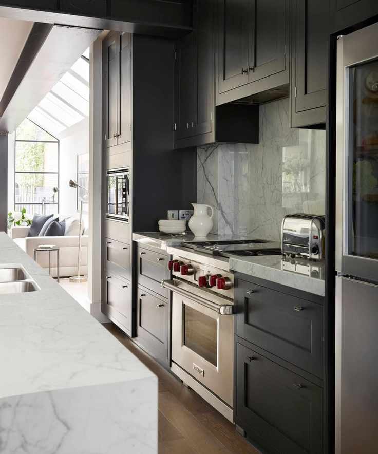 A black galley kitchen with chrome appliances leading into a white living room