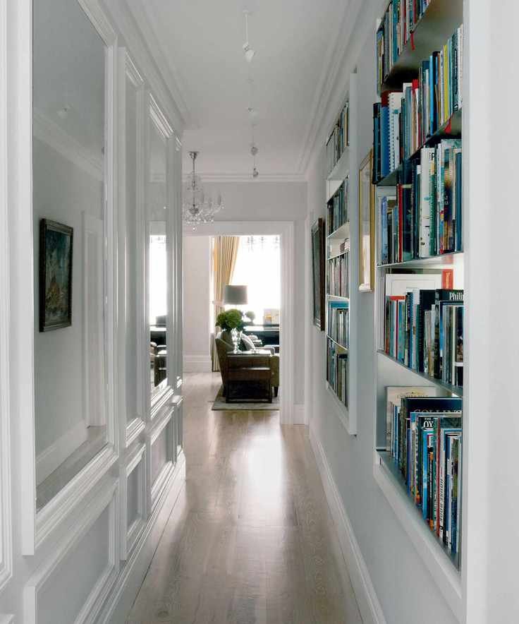 White hallway with built in shelving books mirrored panels suspended spot lighting wooden flooring leading to living room