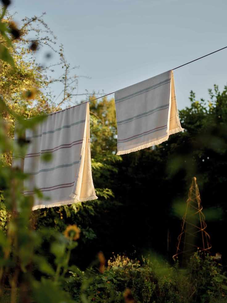 Rowen &amp;amp; Wren Heritage Cotton Bath Towel hanging from a washing line in a golden hour garden surrounded by trees.