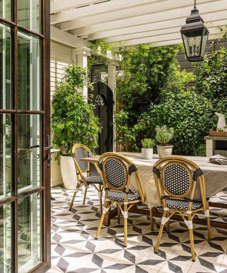 An outdoor dining area with patterned floor tiles and a large white pergola overhead
